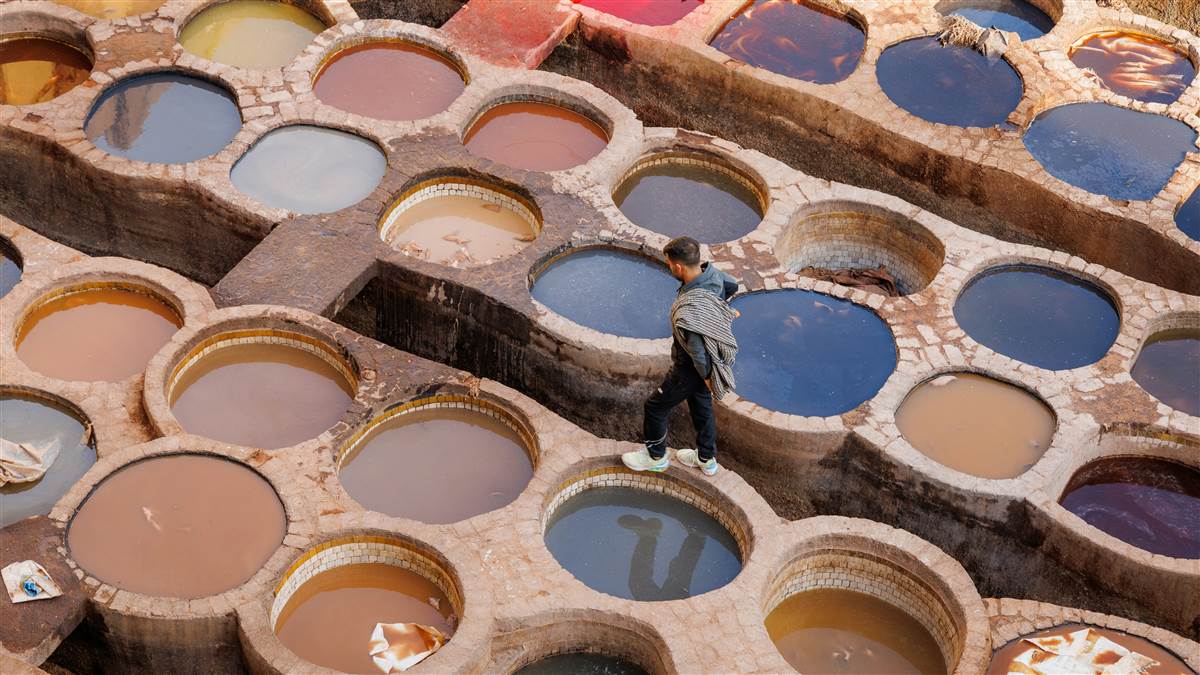 Colorful dye vats of Chouara tannery with worker in Fes medina Morocco