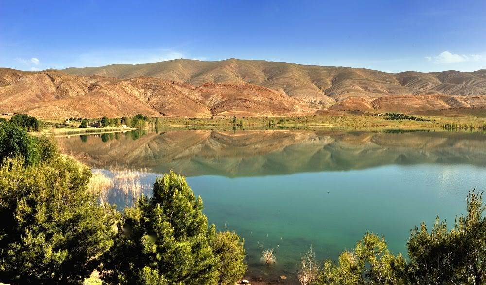 Turquoise Imilchil lake mirroring Atlas mountains, High Atlas Morocco